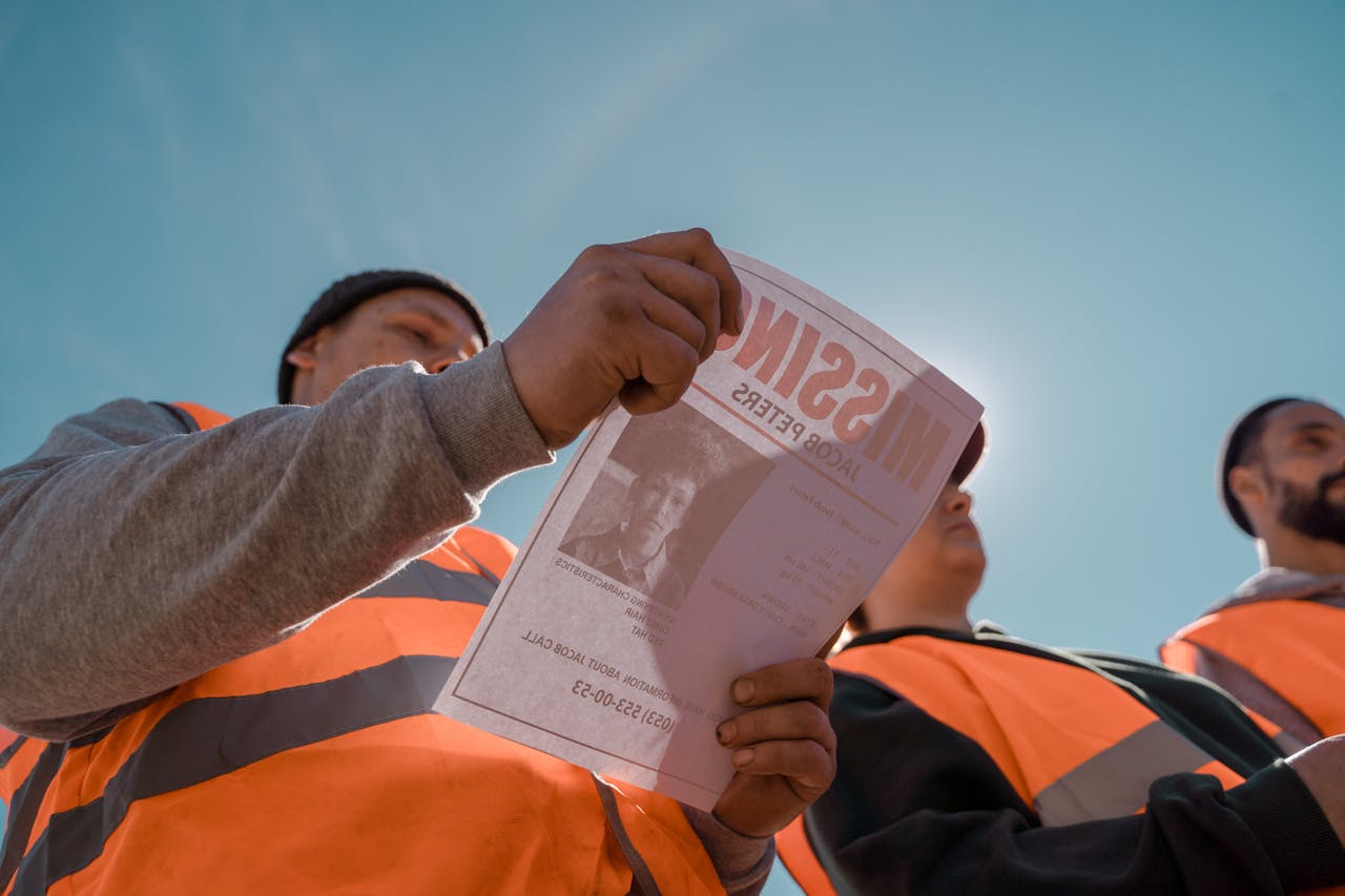 A group of volunteers distributing missing person flyers while conducting a search outdoors in bright daylight.